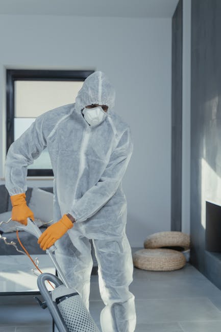 A person wearing bright yellow rubber gloves is cleaning a white wall surface with a blue sponge, while holding a transparent spray bottle filled with cleaning liquid in the other hand. The wall appears smooth and painted white, and the cleaning process is part of surface cleaning or deep cleaning. The scene emphasizes hygiene and maintenance typical of domestic cleaning activities, as performed by Cleaner Highbury, to enhance cleanliness and presentation of residential or commercial spaces.